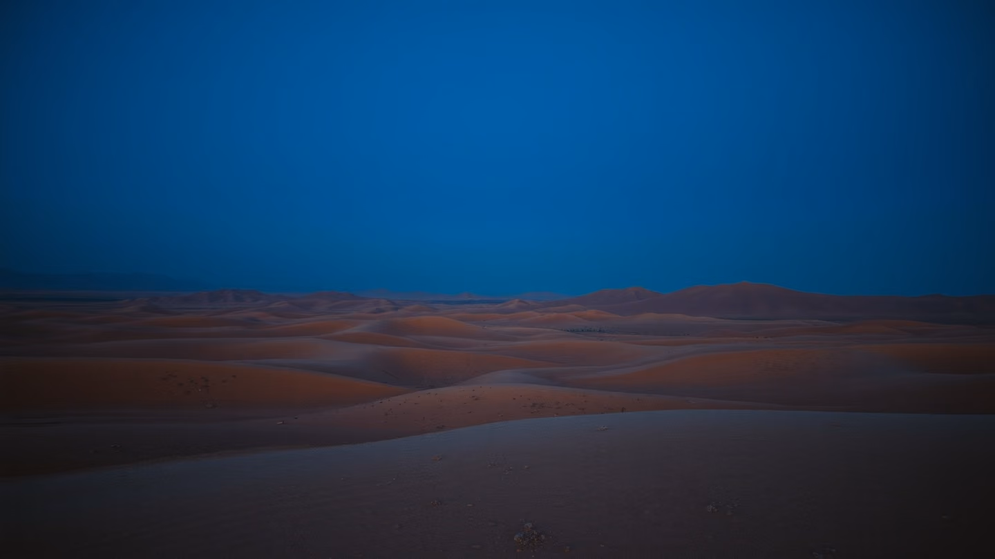 Vast wide shot of a desolate, rolling desert landscape under a deep indigo sky, showing the vast, empty horizon at blue hour.