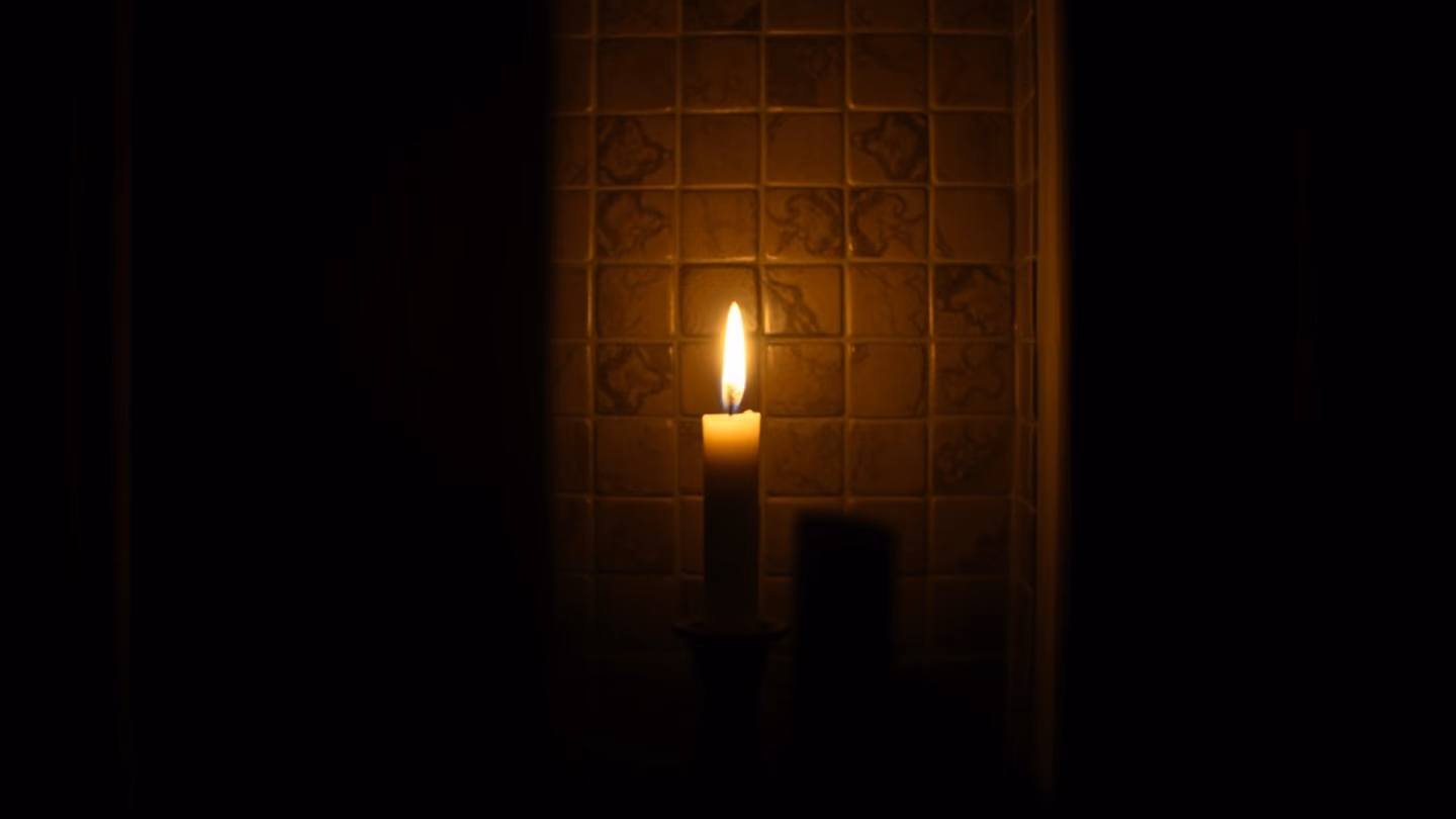 A single ivory candle flickering in a dark hall, casting long, dramatic shadows against a tiled wall, cinematic shallow depth of field.