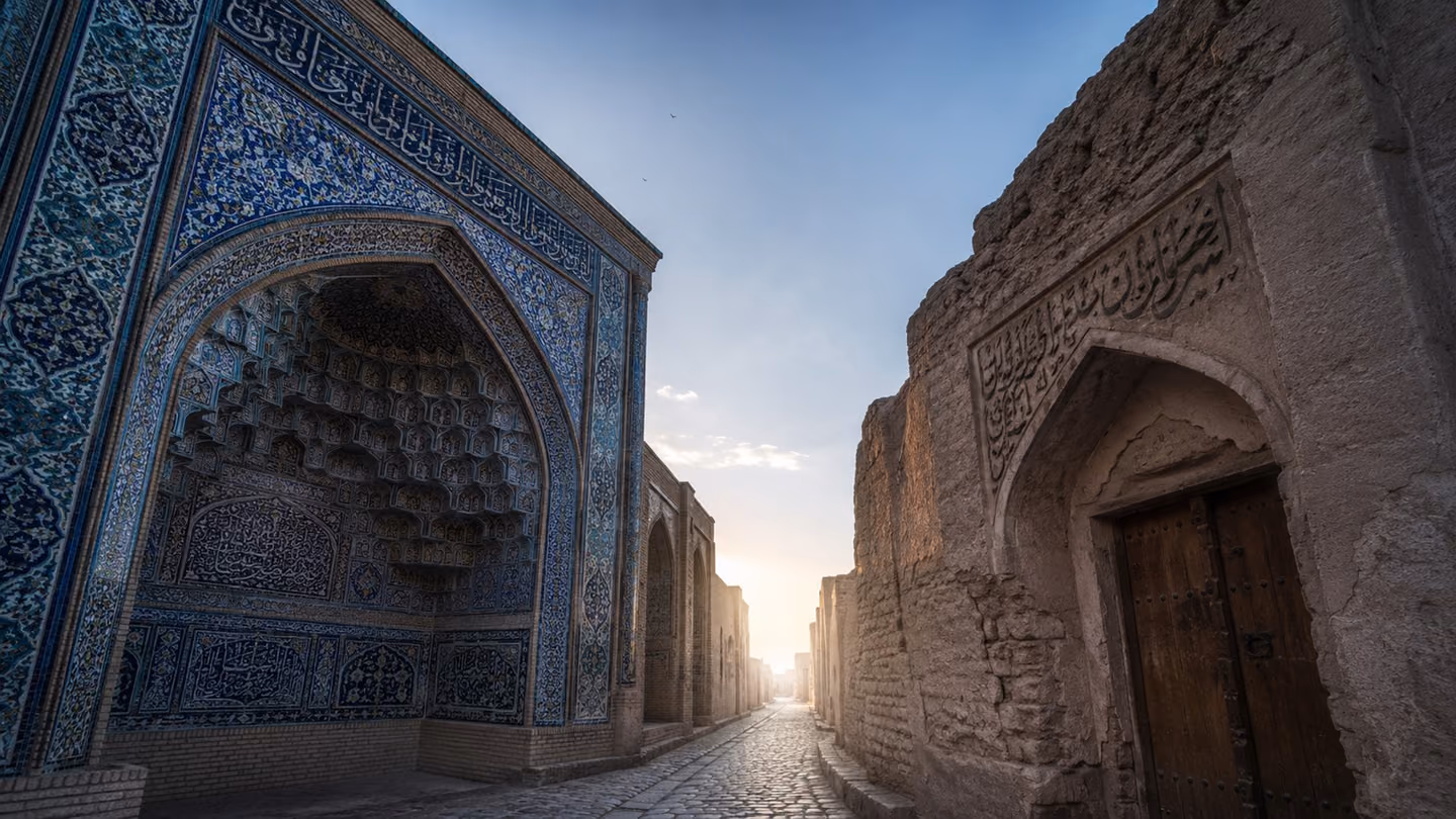An aerial overhead shot looking straight down at the luminous narrow lane between the two closed buildings — the mosque gate to one side, the tavern door to the other — the lane itself glowing with soft white diffused…