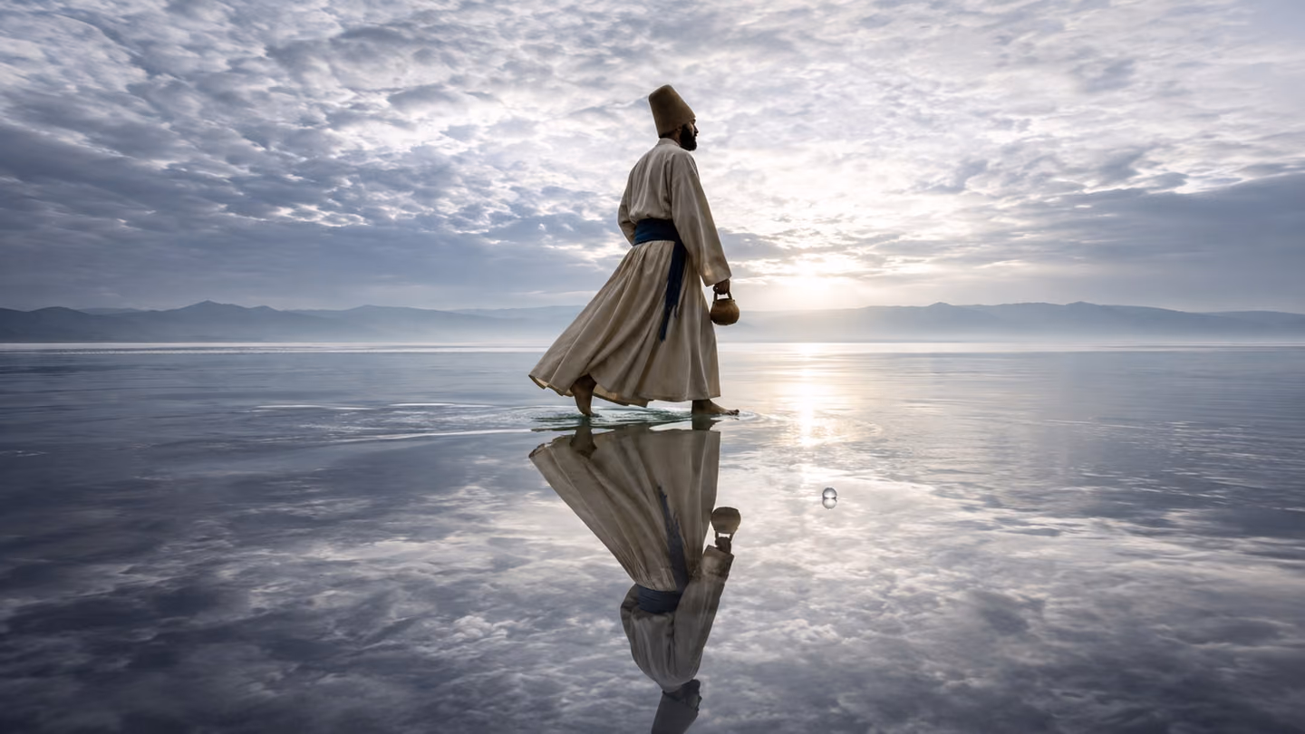 Sweeping low-angle wide shot from just above the waterline of a vast still Persian lake at silver-grey dawn — the seeker, cream-wool khirqa, indigo sash, bare feet, kashkul swinging, wades deliberately into the shallo…