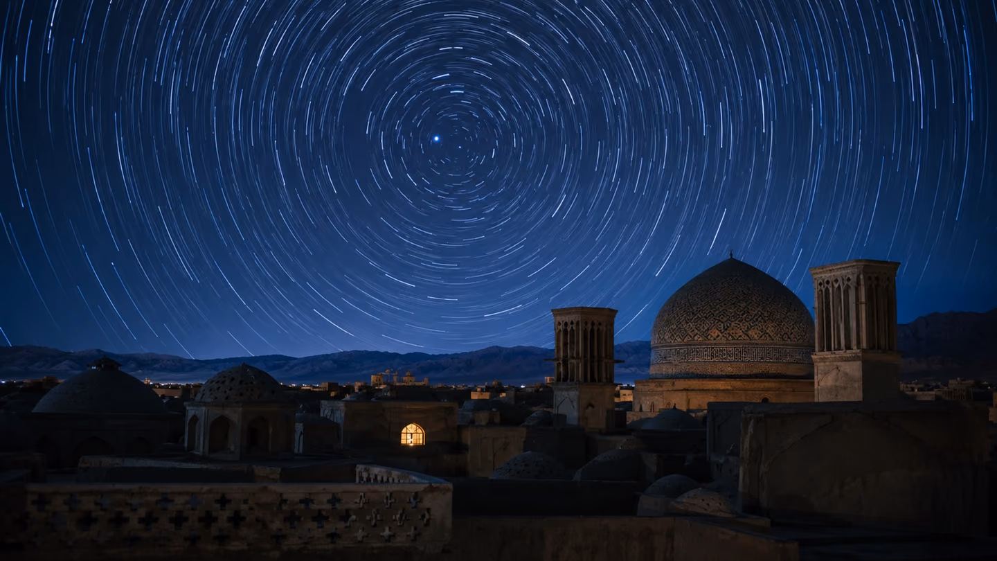 A long-exposure night sky wheeling in slow circular star-trails above the silhouetted dome and wind-towers of an old Shiraz skyline — the heavens visibly turning, rings of light spiralling around the pole star, the to…