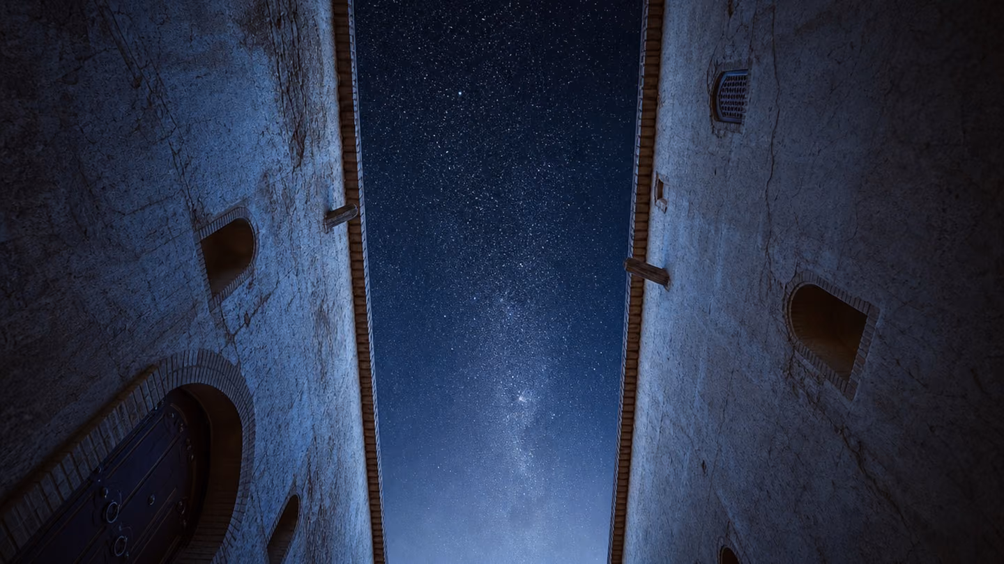 Straight up from the floor of the lane — the camera planted flat on the central river-stone, looking vertically into the full night sky framed perfectly between the two tall plaster walls, stars visible in a deep blue…