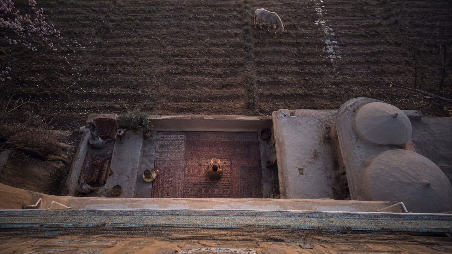 Rain-rinsed rose-earth of a Kashan field takes the print of two open palms; green shoots are already pushing up through the softened ground where the householder kneels, and far across the rows a loose unbroken horse…